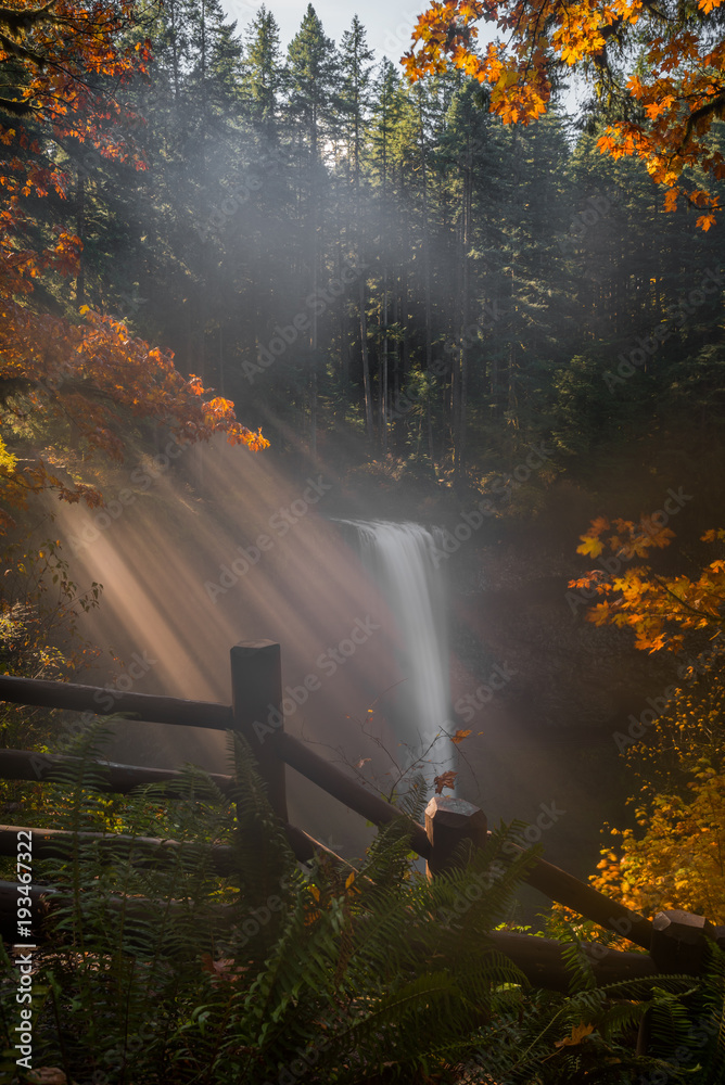 Misty morning light beams over autumn waterfall