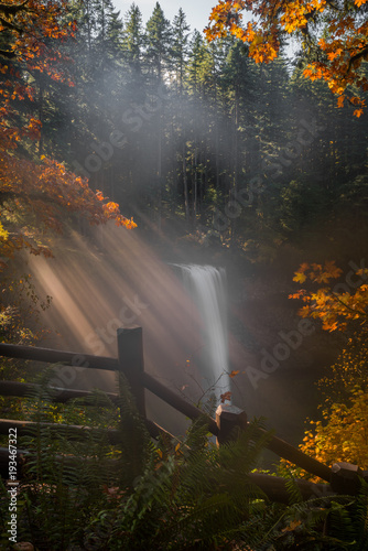 Misty morning light beams over autumn waterfall