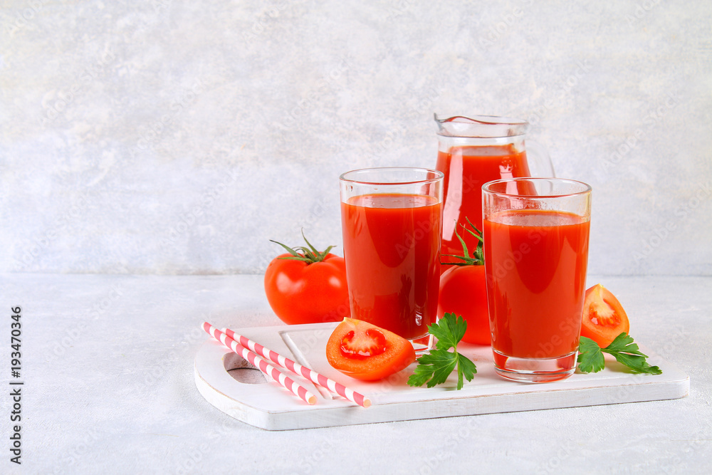 Tomato juice in glasses and a pitcher on a gray concrete table. Tomato juice in glasses and a pitcher on a gray concrete table.