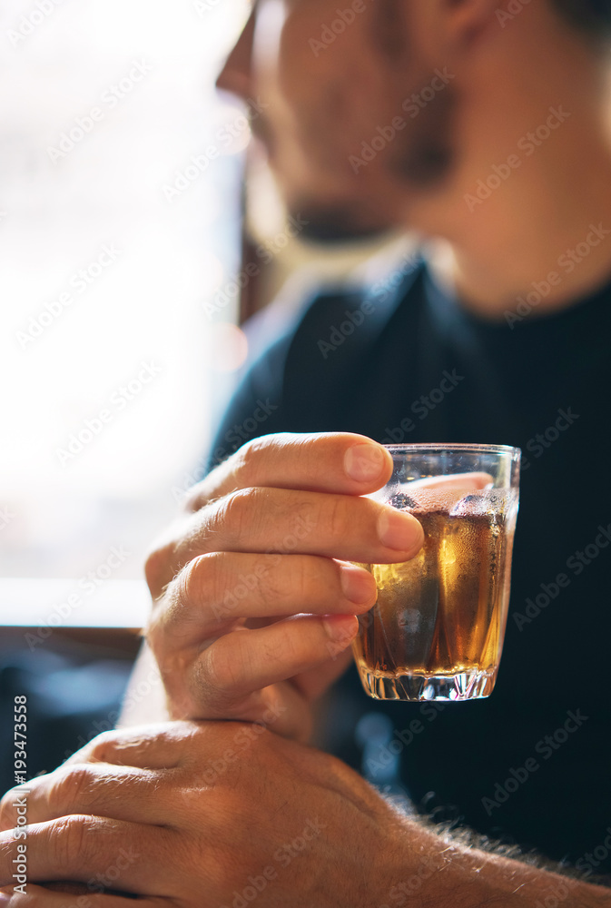 glass with a cold refreshing brown tea in the hand of a man in the background of a cafe. vertical photo.