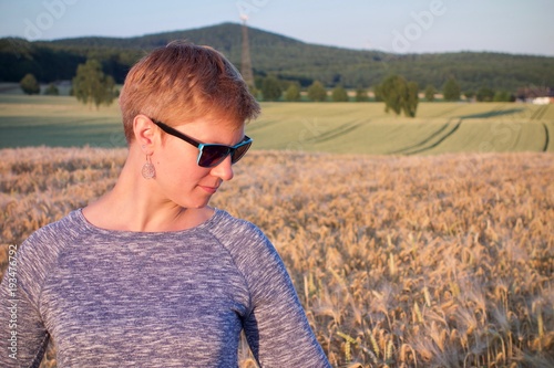 Woman with blue sunnglasses at sunset looking down in a corn field