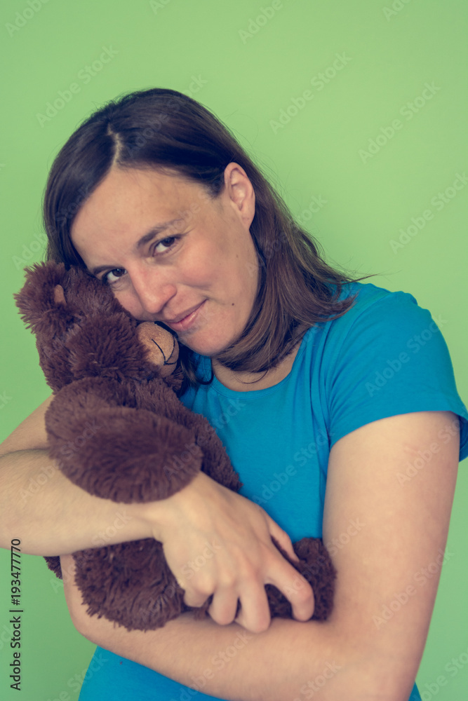 Pregnant woman posing with a plush toy imitating baby in front of green background. Pregnant woman posing with a plush toy imitating baby in front of green background.
