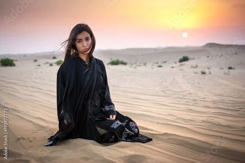 Beautiful young woman in black dress sitting in the desert.