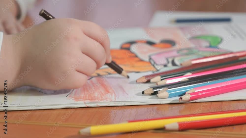 Close-up of unknown little girl draws the pictures using color pencils in the album in the kindergarten Close-up of unknown little girl draws the pictures using color pencils in the album in the kindergarten