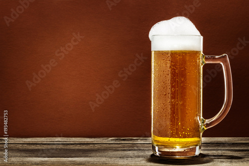 A Glass Of Foaming Beer On A Wooden Table Isolated On Brown Background
