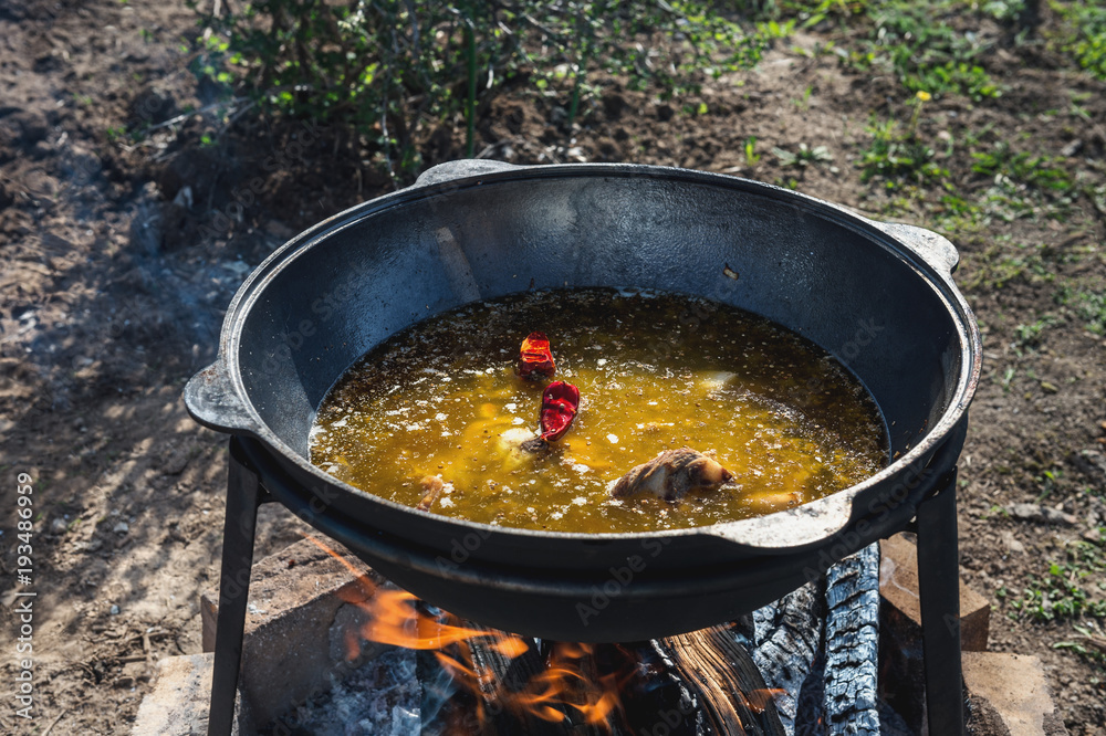 Cooking pilaf in a large cauldron with a strong steaming on an open fire outdoors on a Sunny summer day . Cooking pilaf in a large cauldron with a strong steaming on an open fire outdoors on a Sunny summer day .
