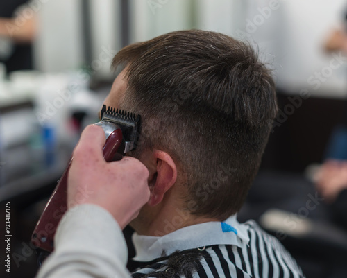 The hands of young barber making haircut to attractive man in barbershop