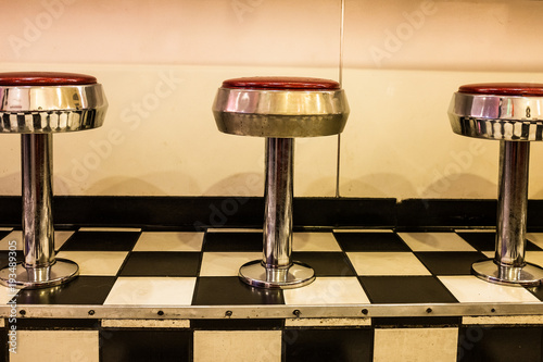 Close up of 50s diner chrome and red stools on black and white checkerboard tiled floor