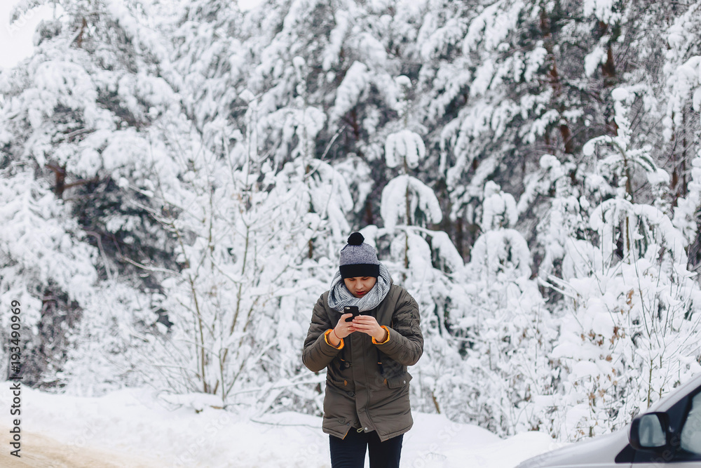 a guy walking along a snow-covered road near a pine forest with phone