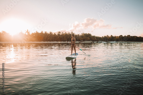 Woman paddleboarding in sea against sky during sunset