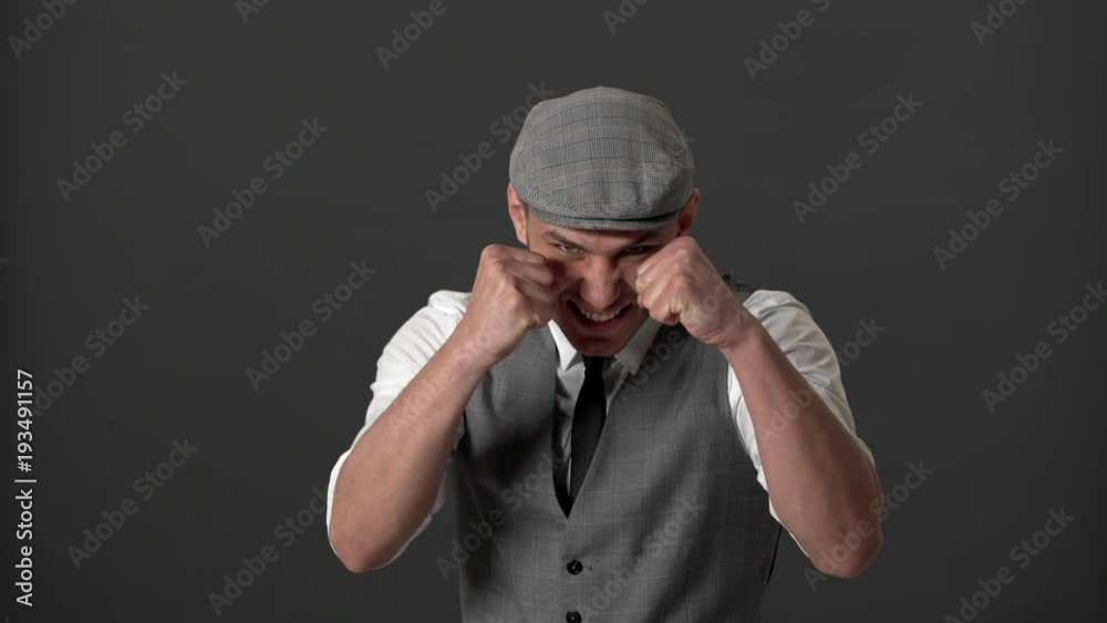 Portrait of dangerous gangster guy in suit and flat cap fighting and clenching fists in defense position, over gray wall. Concept of emotions Portrait of dangerous gangster guy in suit and flat cap fighting and clenching fists in defense position, over gray wall. Concept of emotions