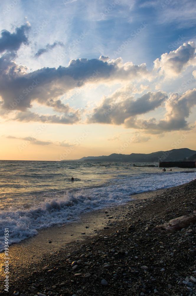 Amazing sea sunset on the pebble beach, the sun, waves, clouds