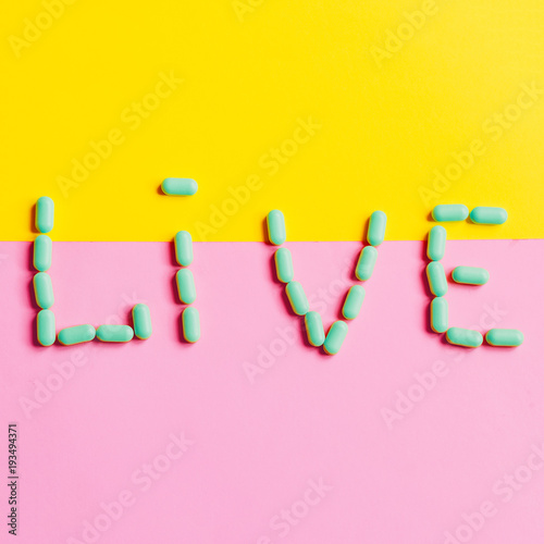 Live. yellow and pink background. square. the word is laid out of the tablets.