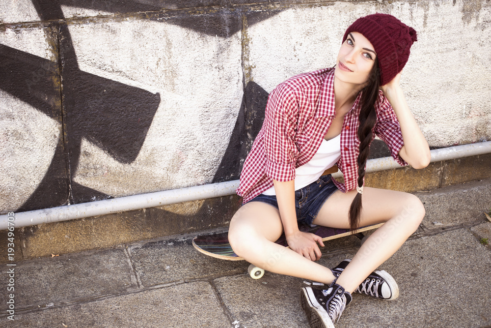 Brunette teenage girl in hipster outfit (jeans shorts, keds, plaid shirt,  hat) with a skateboard at the park outdoors Stock Photo | Adobe Stock