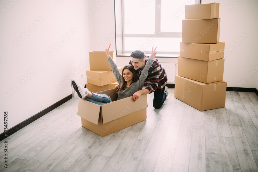 Fototapeta premium The young woman sitting in a cardboard box. Moving, purchase of new habitation.