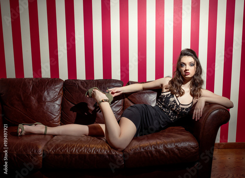 A young girl in a tight black dress sits on the couch. Leather sofa