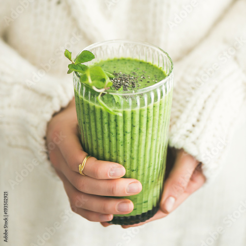 Matcha green vegan smoothie with chia seeds and mint in glass in hands of female wearing white sweater, square crop. Clean eating, detox, alkaline diet, weight loss concept