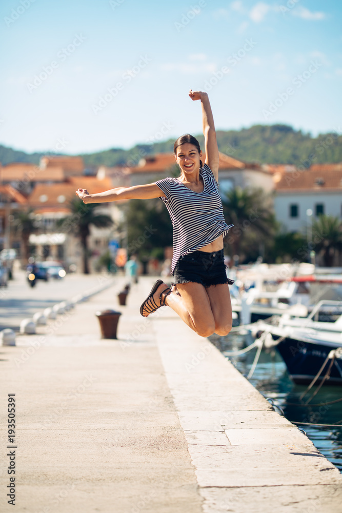 Over exited happy woman jumping in the air out of happiness.Vacation time concept.Seaside coastal vacation excitement.Woman in joy got good news.Rejoicing,full of life.Summer female active,energetic