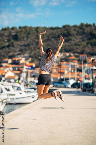 Over exited happy woman jumping in the air out of happiness.Vacation time concept.Seaside coastal vacation excitement.Woman in joy got good news.Rejoicing,full of life.Summer female active,energetic