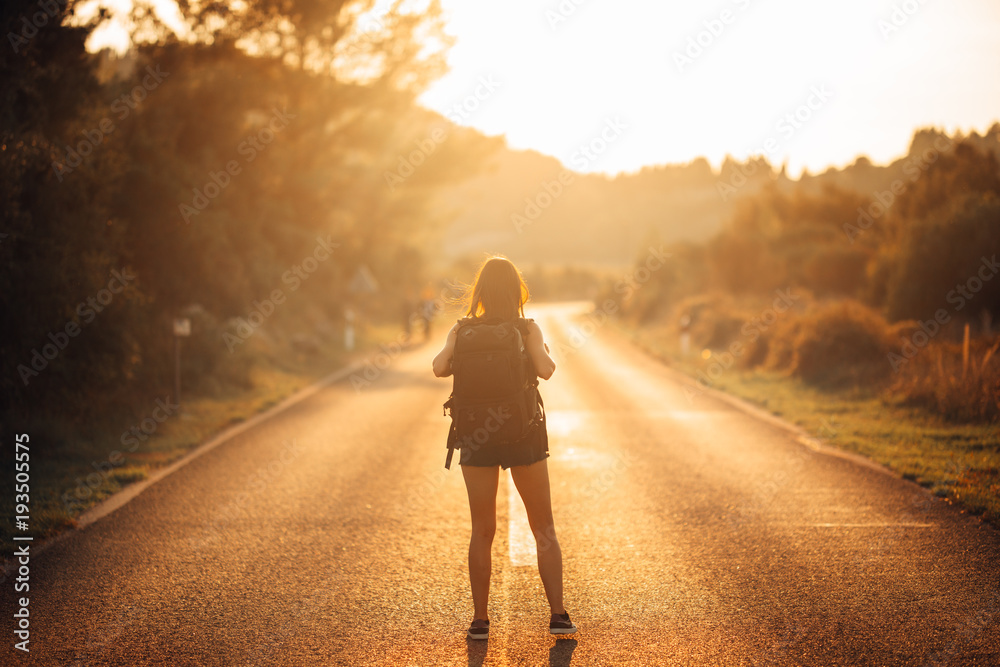 Young backpacking adventurous woman hitchhiking on the road.Ready for adventure of life.Travel lifestyle.Low budget traveling.Adventurous active vacations.Hitchhiking tourism concept.Backpacker