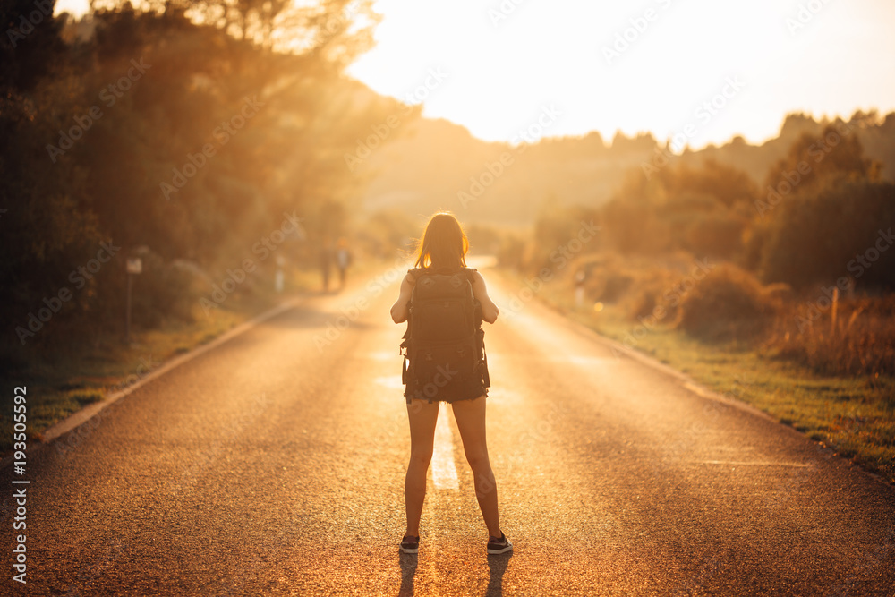 Young backpacking adventurous woman hitchhiking on the road.Ready for adventure of life.Travel lifestyle.Low budget traveling.Adventurous active vacations.Hitchhiking tourism concept.Backpacker
