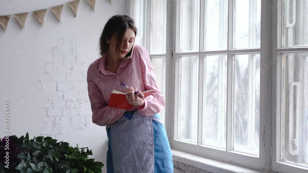 Professional florist speaks on the phone and writing notes to the notebook. Professional florist speaks on the phone and writing notes to the notebook.