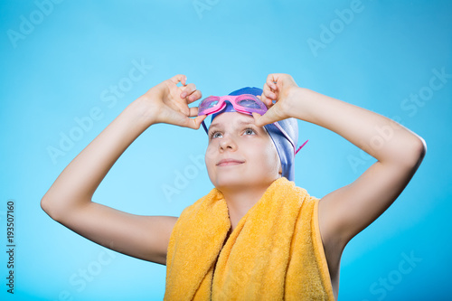 Girl swimmer in a bathing cap and glasses. The girl holds glasses for diving. She looks up.