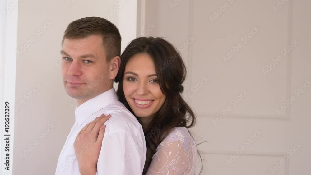 young couple in background white wall man in a suit girl with brakits in a tender serene dress will smile into the camera and smile in an embrace. young couple in background white wall man in a suit girl with brakits in a tender serene dress will smile into the camera and smile in an embrace.