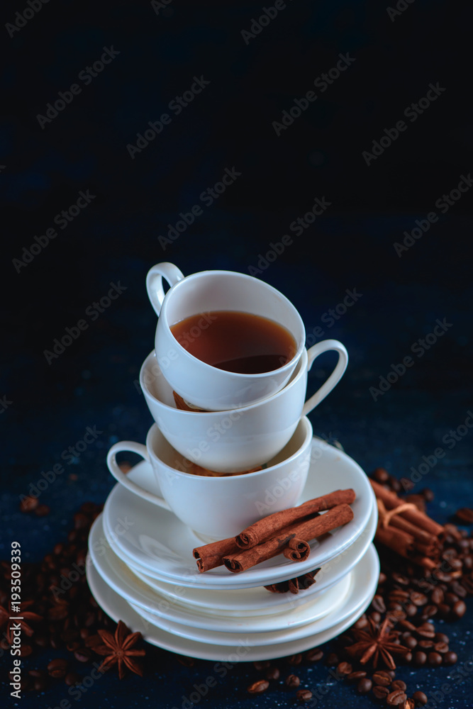 Obraz premium Close-up of a pile of dishes and cups with coffee beans and cinnamon on a dark blue background. Creative barista concept with copy space.