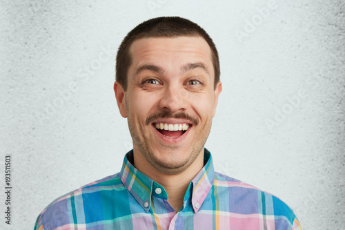 Stylish man with dark warm eyes and mustache smilig into the camera. Happy and glad to have a new car. Wearing colorful shirt. Isolated over white studio wall. photo