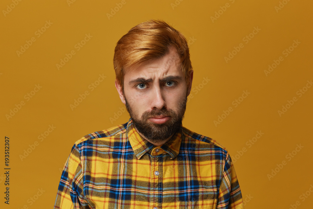 Stressed frustrated male curves lower lip, wears yellow shirt  and looks displeased into camera. Yellow background. Depression and unhappy