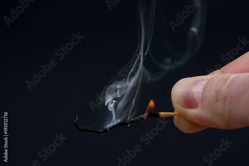 Burning and Smoking wooden match in hand on dark background.
