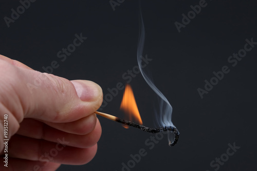 Burning and Smoking wooden match in hand on dark background.
