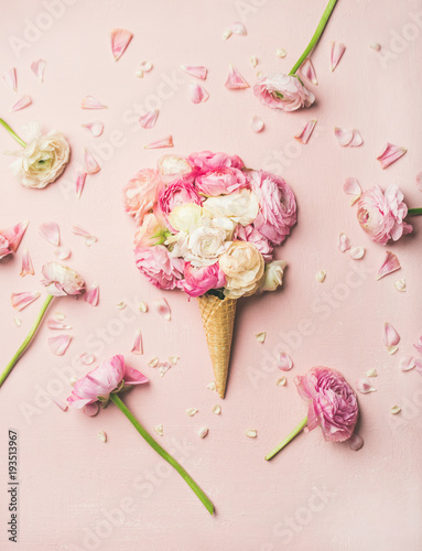 Flat-lay of waffle sweet cone with pink and white buttercup flowers over pastel light pink background, top view. Spring or summer mood concept