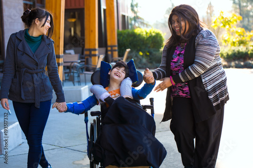 Disabled boy in wheelchair holding hands with caregivers on walk