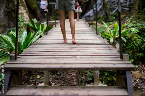 Thai women barefoot walking on wood bridge.