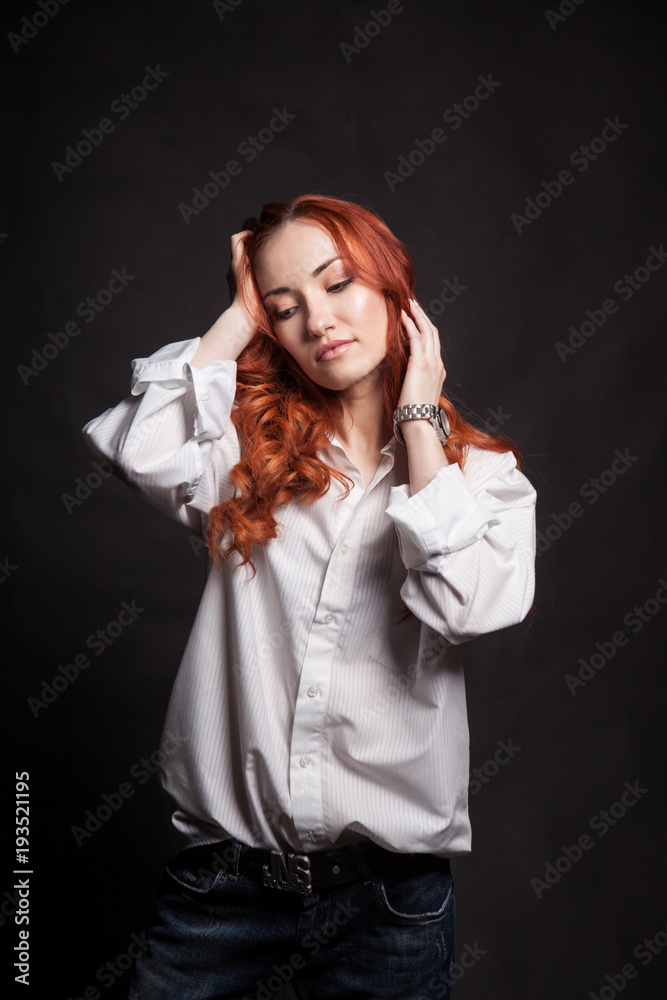Portrait of a beautiful girl with long red hair in a white man's shirt on a dark background in the studio Portrait of a beautiful girl with long red hair in a white man's shirt on a dark background in the studio