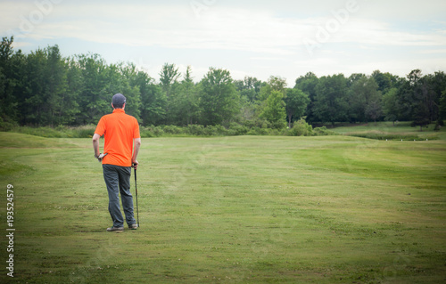 Golfer looking down a wide open fairway and leaning on his golf club