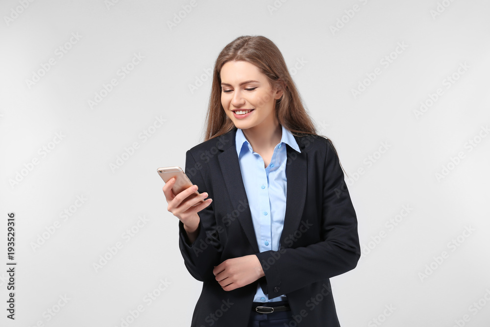 Beautiful young woman in elegant suit and with mobile phone on light background Beautiful young woman in elegant suit and with mobile phone on light background