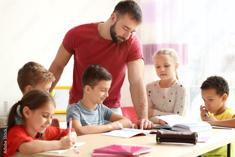 Male teacher helping children with homework in classroom at school Male teacher helping children with homework in classroom at school