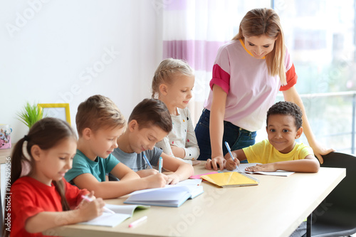 Female teacher helping children with homework in classroom at school