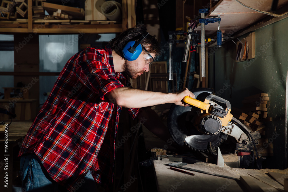 brunette man profession carpenter builder saws with a circular saw a wooden board.