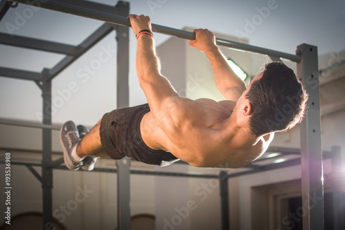 Handsome muscular man doing exercises on horizontal bar outdoors. Calisthenics workout. photo