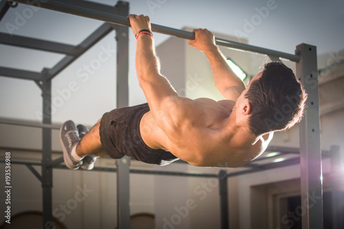 Obraz na plátně Handsome muscular man doing exercises on horizontal bar outdoors
