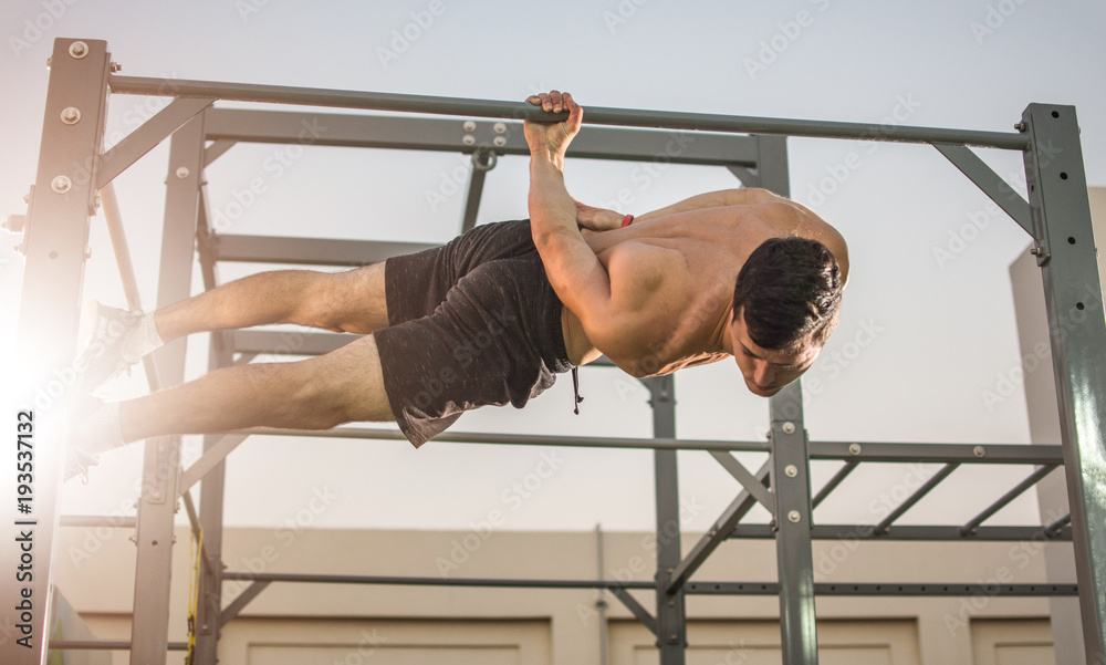 Muscular man doing exercises on horizontal bar hanging on one hand.  Calisthenics workout. Stock-Foto | Adobe Stock