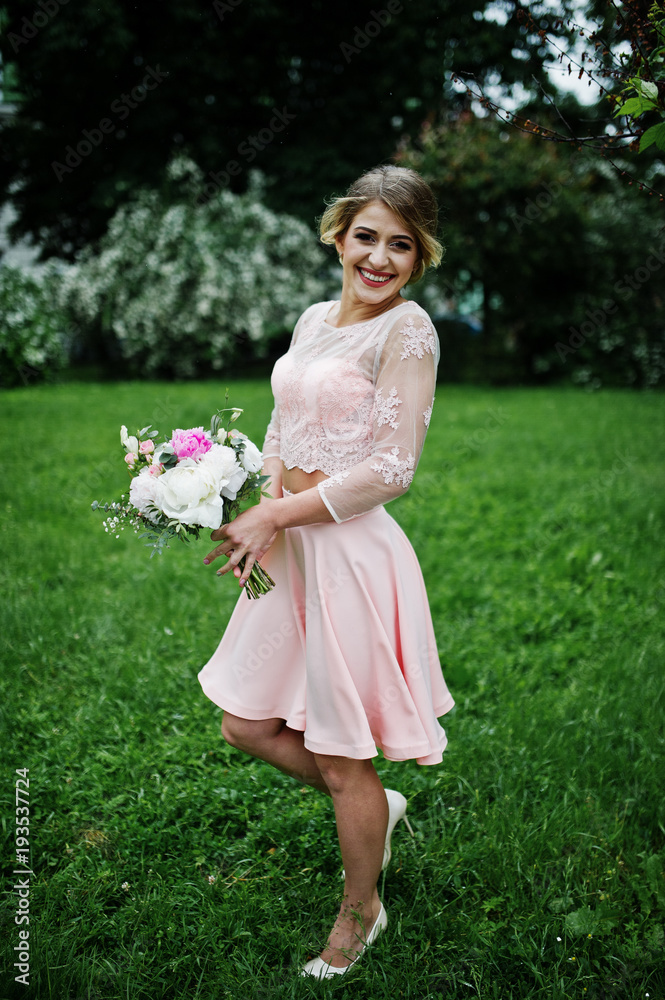 Perfect girl in pink dress with bouquet at hands.