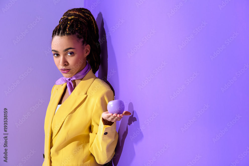 african american girl posing in yellow suit with purple apple, on trendy ultra violet background african american girl posing in yellow suit with purple apple, on trendy ultra violet background