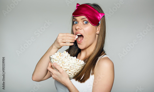 Woman eating popcorn in the night. Girl wearing pink sleep mask.