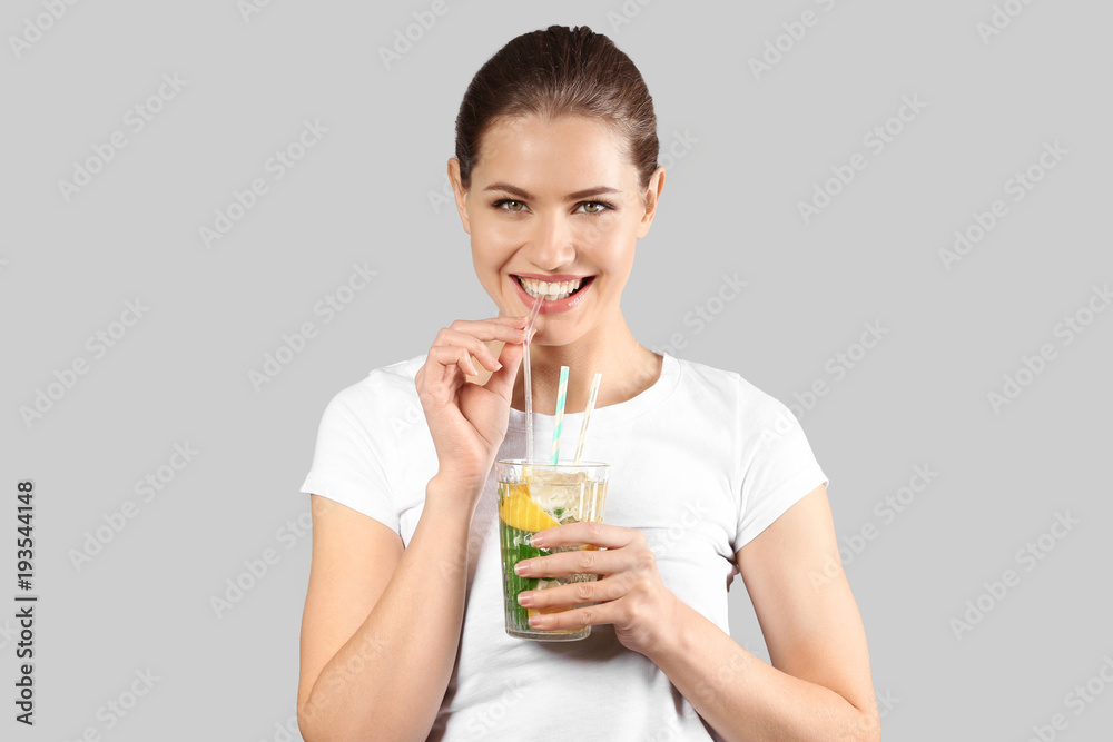 Beautiful young woman drinking lemonade on grey background Beautiful young woman drinking lemonade on grey background