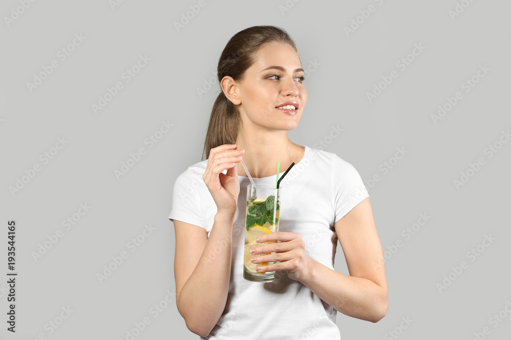Beautiful young woman with glass of lemonade on grey background Beautiful young woman with glass of lemonade on grey background